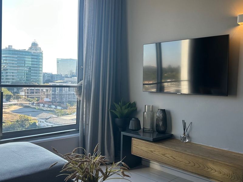 A modern living room featuring a floating media console, wall-mounted lighting, and floor-to-ceiling windows offering expansive city views.