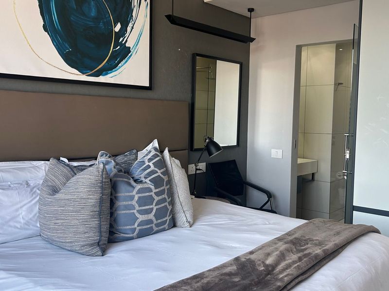 Modern bedroom featuring an upholstered headboard, built-in wardrobe, and direct access to an en-suite bathroom with contemporary finishes.