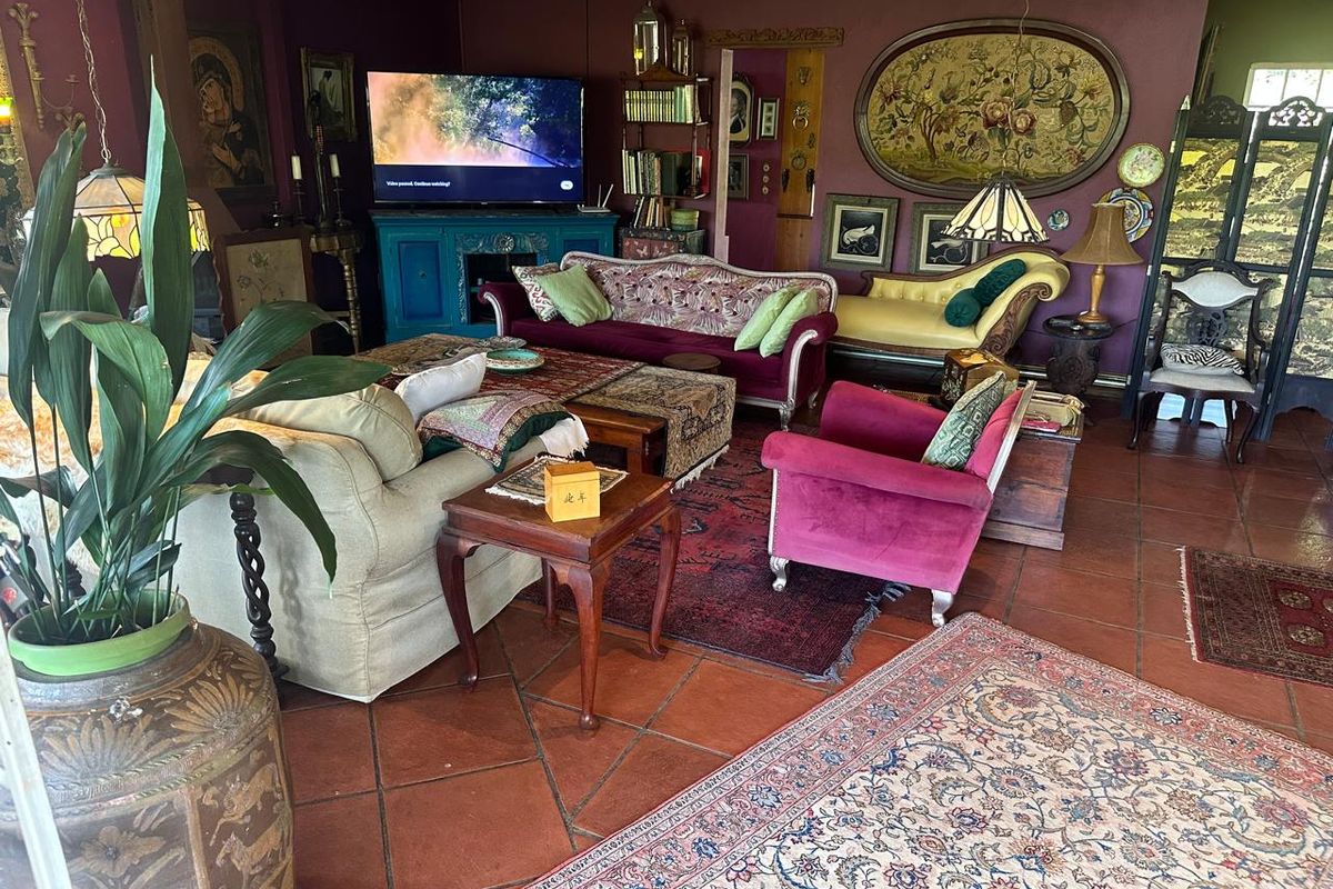 A spacious living room featuring traditional terracotta floor tiles and a drop ceiling, currently styled with eclectic decor and furnishings.