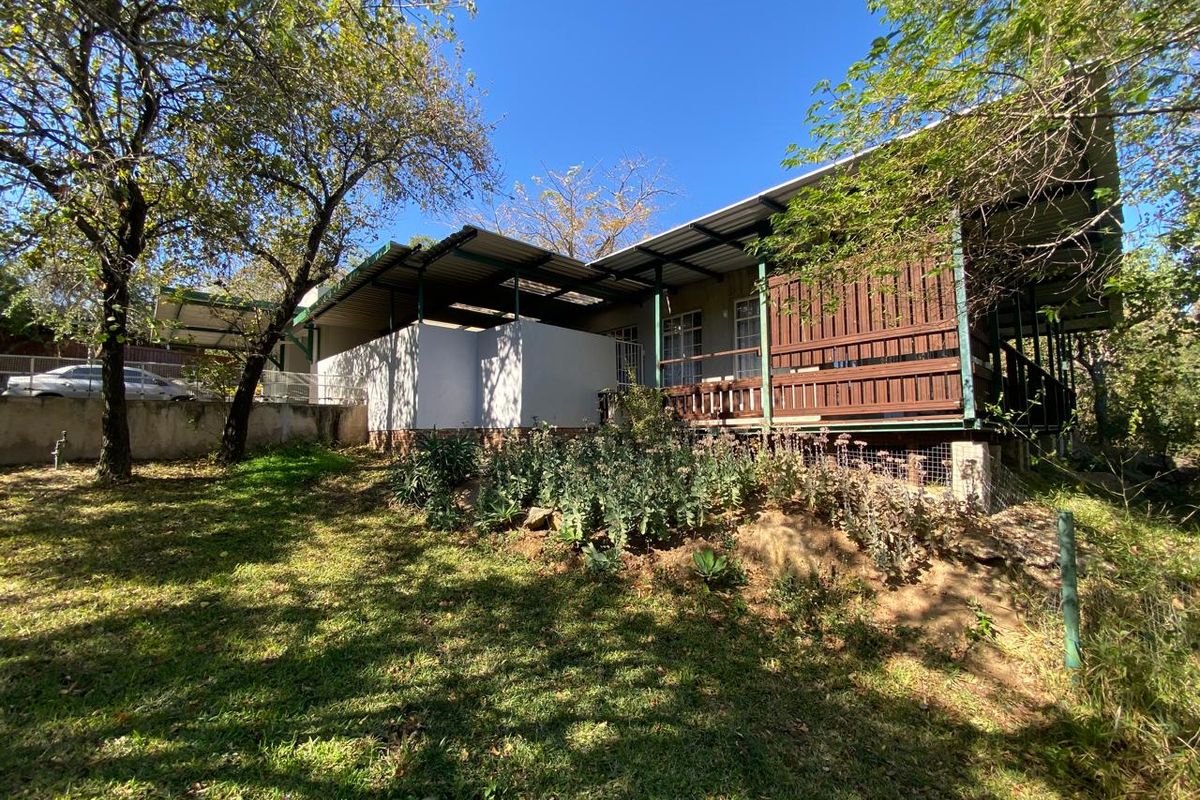 Rear view of the property featuring a raised timber deck, corrugated metal roofing, and established garden surroundings.