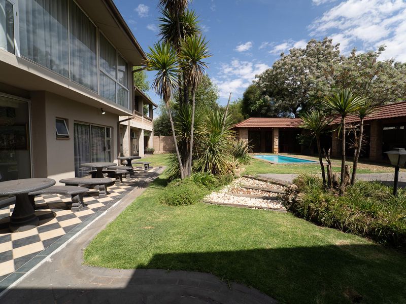Spacious rear garden featuring a swimming pool, landscaped lawn, stone steps, and a tiled patio area adjacent to the main building.