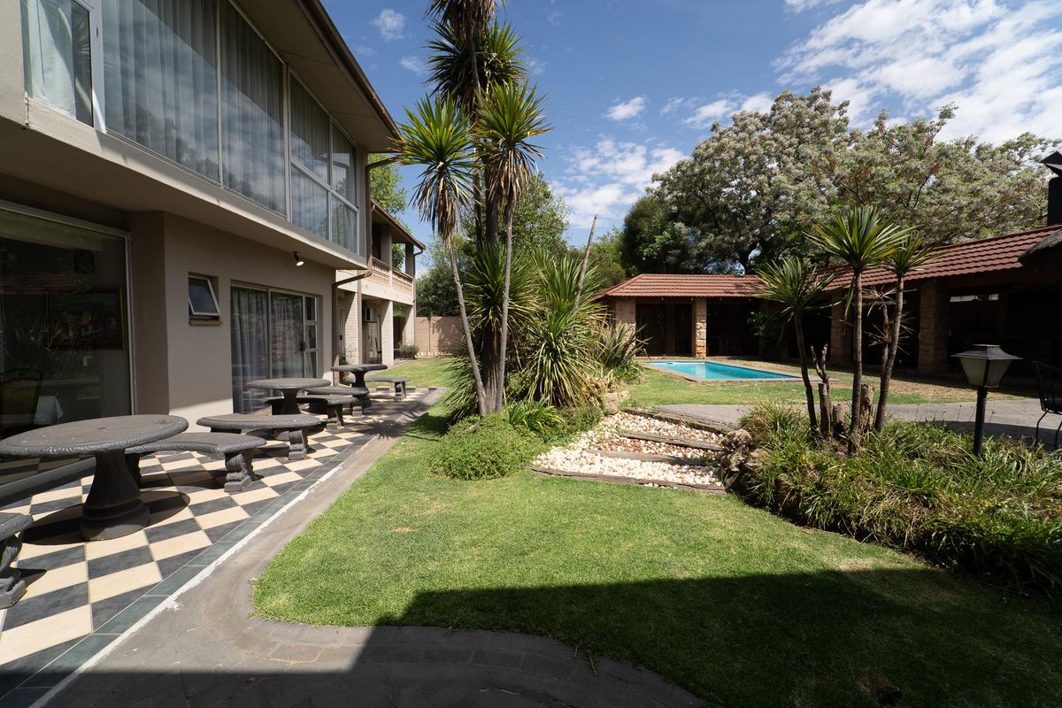 Spacious rear garden featuring a swimming pool, landscaped lawn, stone steps, and a tiled patio area adjacent to the main building.