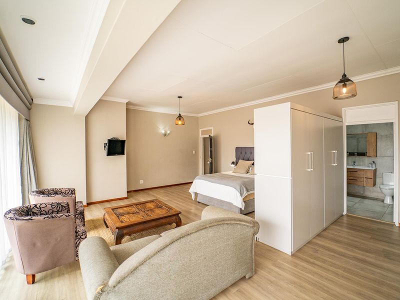 Spacious bedroom featuring laminate flooring, recessed and pendant lighting, a built-in wardrobe, and an attached en-suite bathroom.
