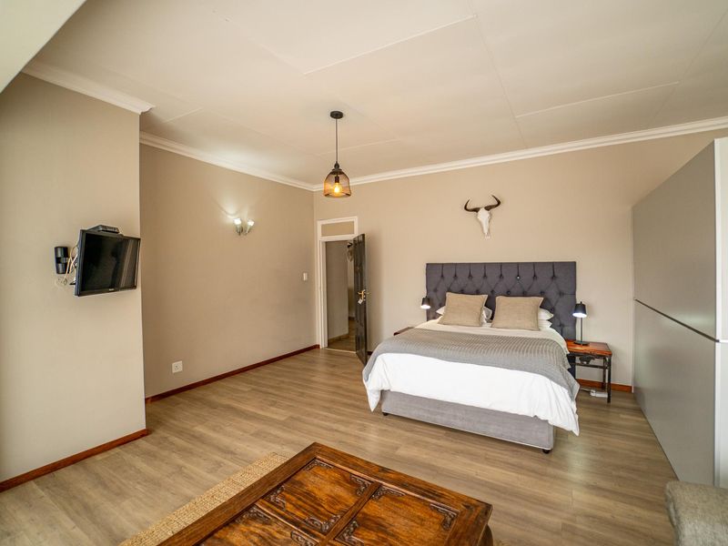 A spacious bedroom featuring modern laminate flooring, neutral wall tones, built-in wardrobe storage, and elegant lighting fixtures.