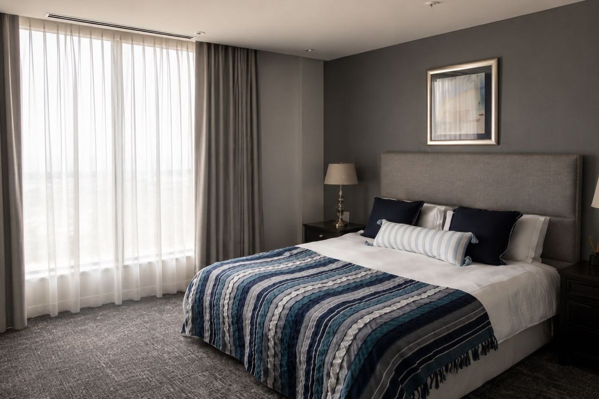 A well-appointed bedroom featuring floor-to-ceiling windows, recessed ceiling lighting, and integrated ducted air conditioning, finished with neutral tones and high-quality fixtures.