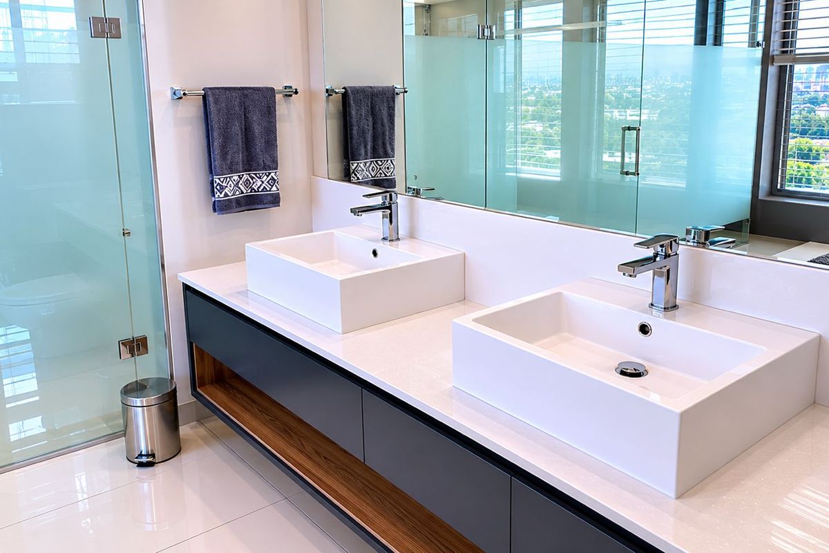 Modern penthouse bathroom featuring a sleek double vanity with vessel sinks, quartz countertops, and a spacious glass-enclosed shower with city views.