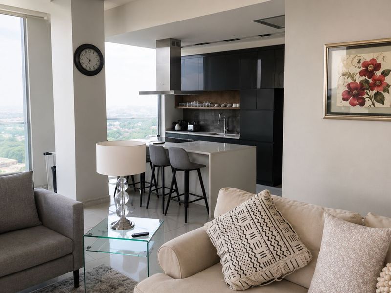 Modern open-plan penthouse living area featuring a sleek kitchen with island, high-end cabinetry, and expansive floor-to-ceiling windows offering panoramic city views.