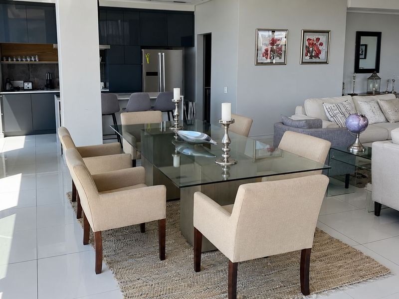 Spacious open-plan living and dining area featuring modern glossy kitchen cabinetry, large format floor tiles, and expansive floor-to-ceiling windows with abundant natural light.
