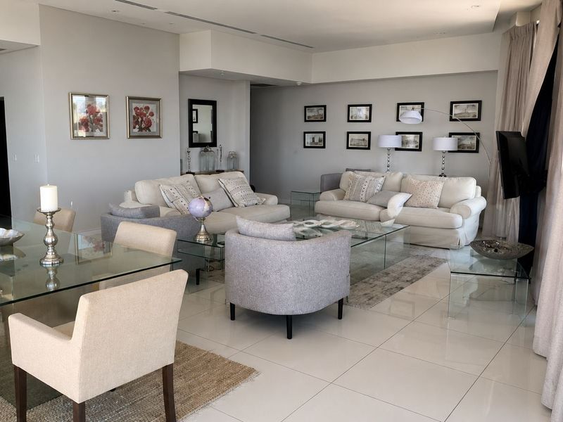 Spacious open-plan living and dining area featuring polished porcelain flooring, recessed lighting, and a modern integrated kitchen, flowing seamlessly to large glass balcony doors.