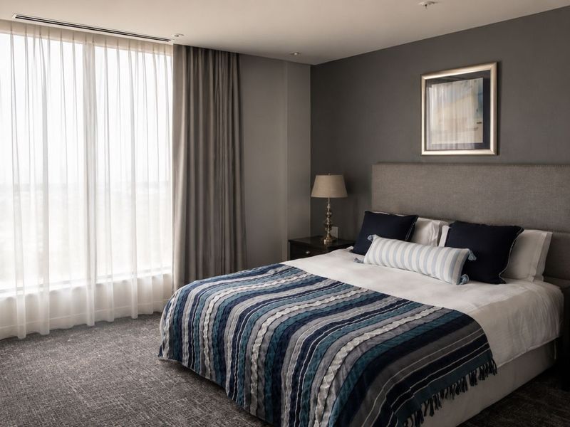 A well-appointed bedroom featuring floor-to-ceiling windows, recessed ceiling lighting, and integrated ducted air conditioning, finished with neutral tones and high-quality fixtures.