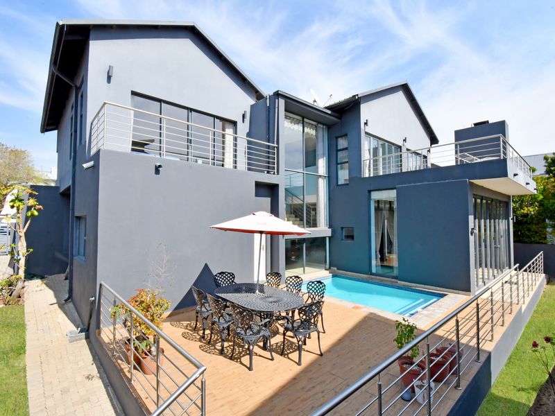 Rear view of a modern double-story house featuring a swimming pool, timber deck, and upper-level balconies with stainless steel railings.