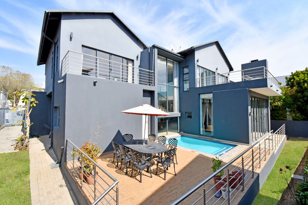 Rear view of a modern double-story house featuring a swimming pool, timber deck, and upper-level balconies with stainless steel railings.