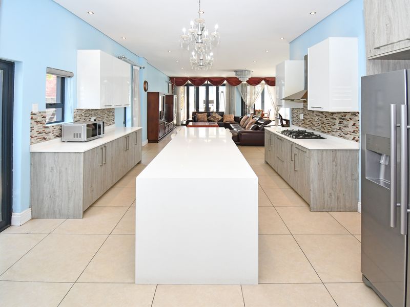 Spacious open-plan kitchen featuring a large central island, modern cabinetry, quartz countertops, and a mosaic backsplash, flowing into the living area.