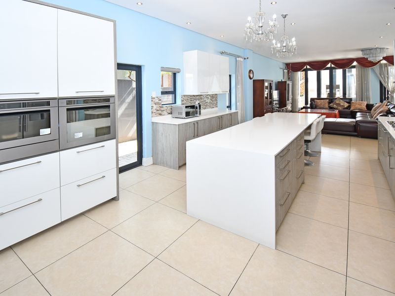 Spacious open-plan kitchen and living area featuring a large central island, modern built-in appliances, stone countertops, and large format floor tiles.