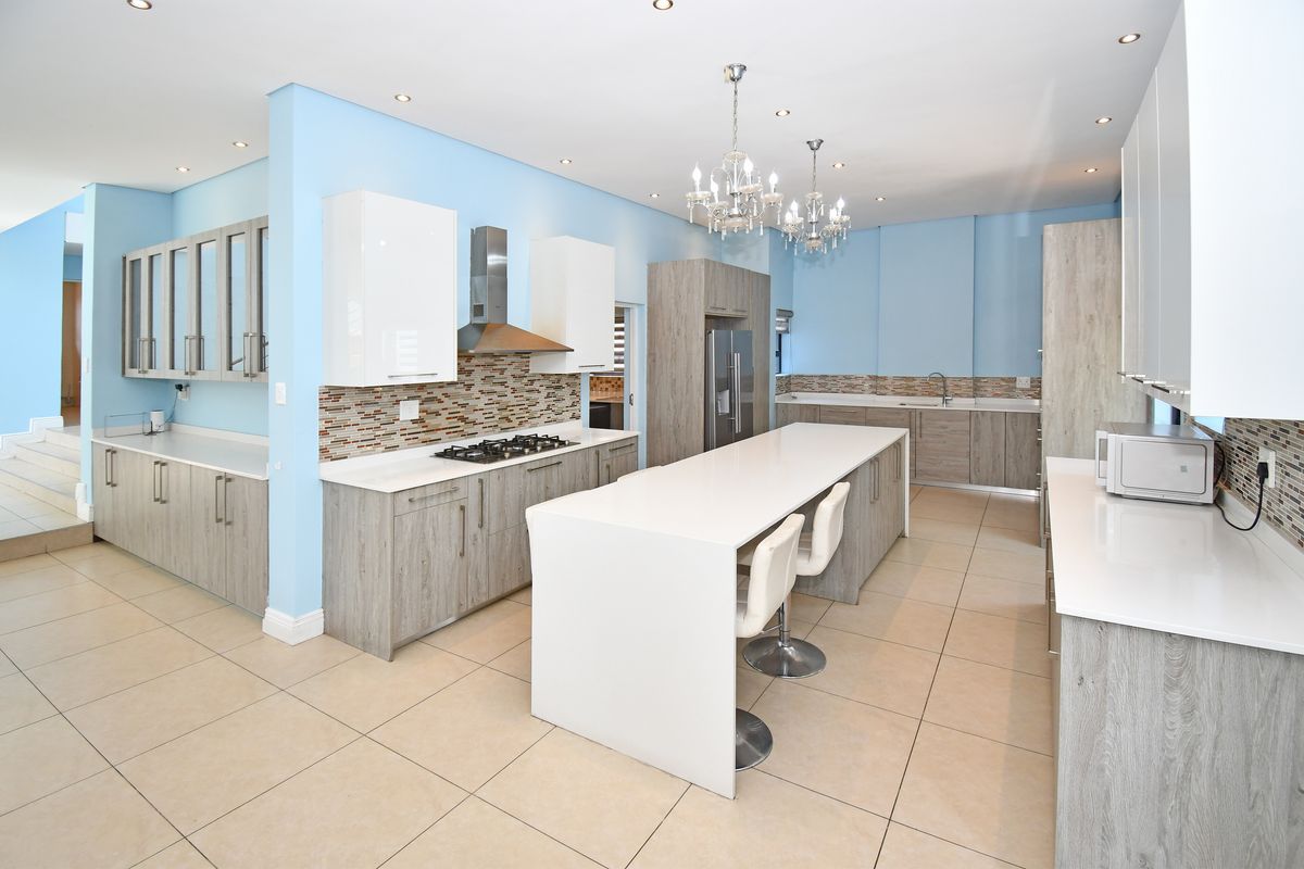 Modern kitchen featuring a large central island, stone countertops, gas hob, extractor fan, and ample built-in cabinetry with a light blue accent wall.