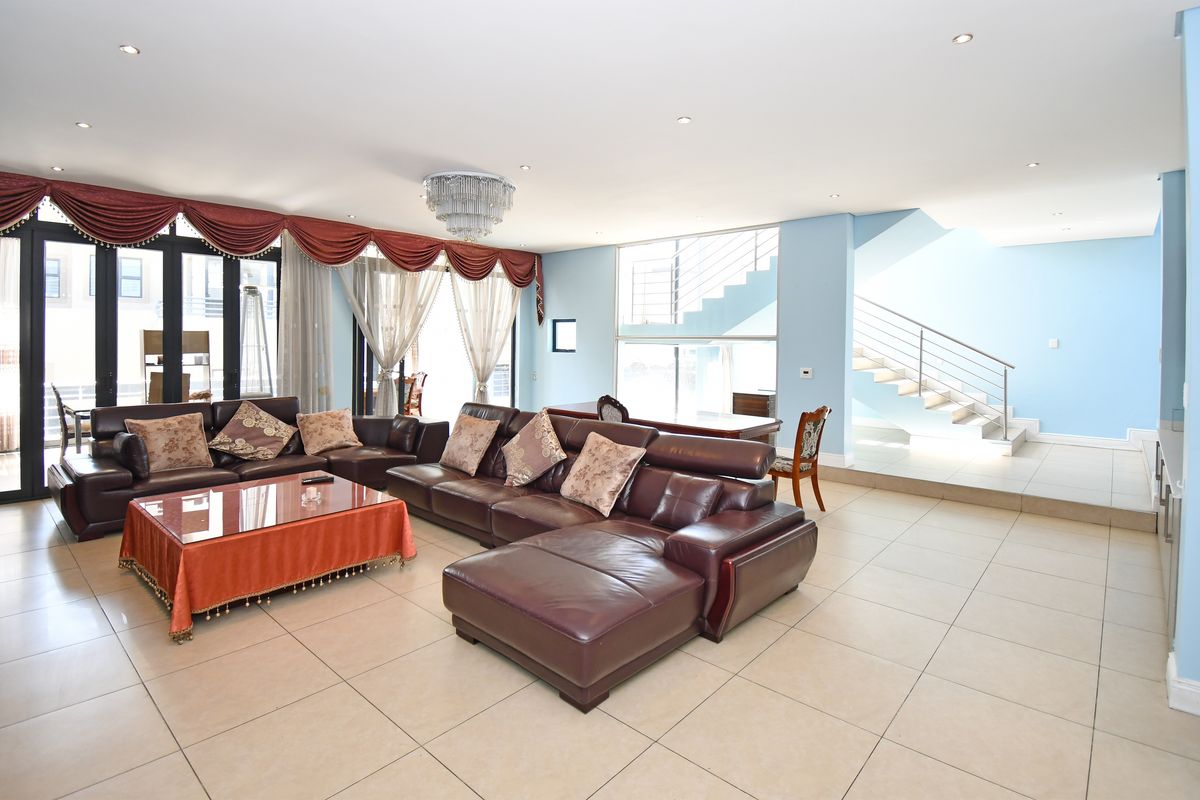 Spacious open-plan living area featuring large glass sliding doors, tiled flooring, recessed lighting, and a feature staircase with a modern metal balustrade.