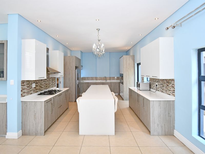 Modern kitchen featuring a central island, stone countertops, gas hob, extractor fan, and mosaic tile backsplash with ample cabinetry.
