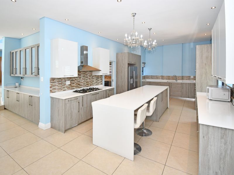 Modern kitchen featuring a large central island, stone countertops, gas hob, extractor fan, and ample built-in cabinetry with a light blue accent wall.