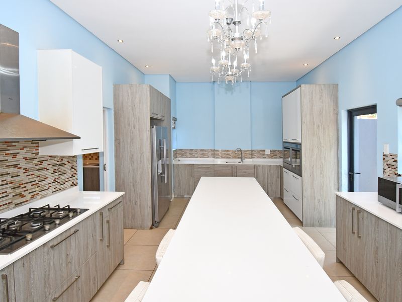 Modern kitchen featuring a central island, quartz countertops, gas hob, stainless steel extractor, and ample built-in cabinetry with a tiled backsplash.