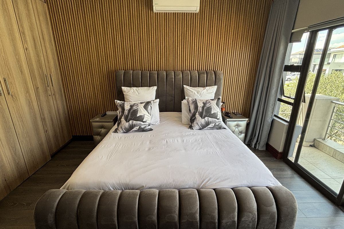 Modern bedroom featuring timber slat wall paneling, built-in wardrobes, laminate flooring, and a sliding glass door providing access to a balcony.