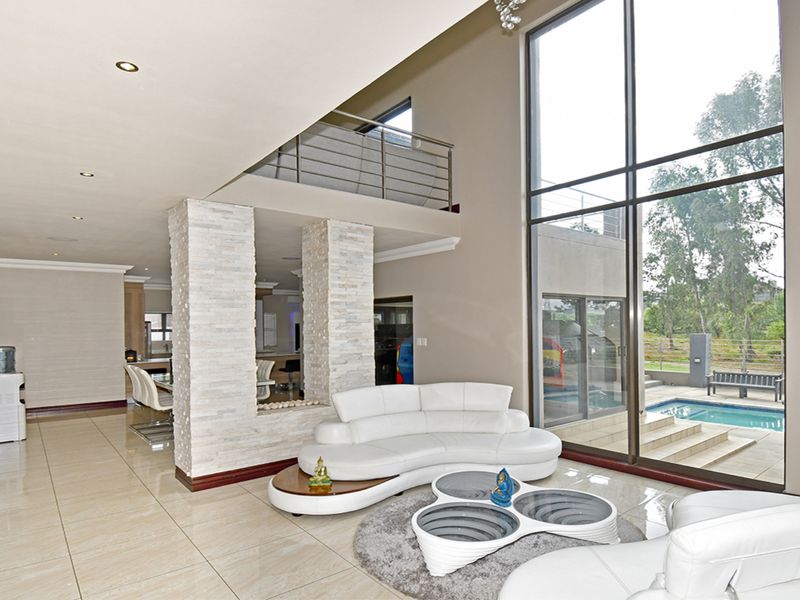 Spacious open-plan living area featuring double-volume windows, a stone-clad feature pillar, and a mezzanine level overlooking the pool area.