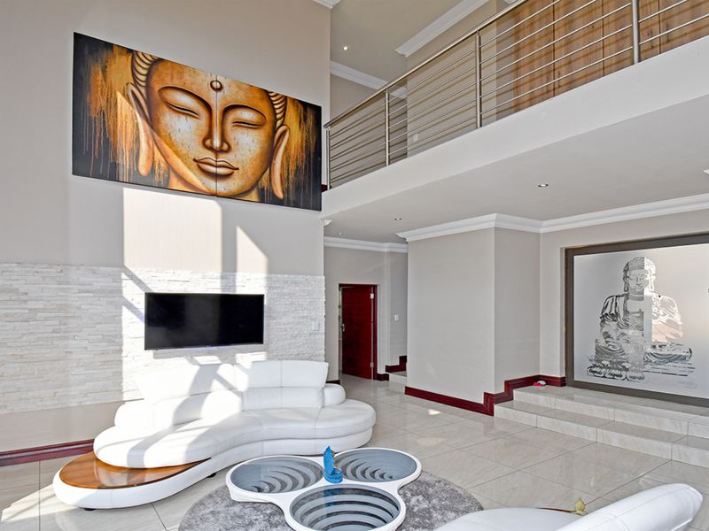 Spacious double-volume living area featuring a stacked stone feature wall, tiled flooring, and a mezzanine level with a modern stainless steel balustrade.