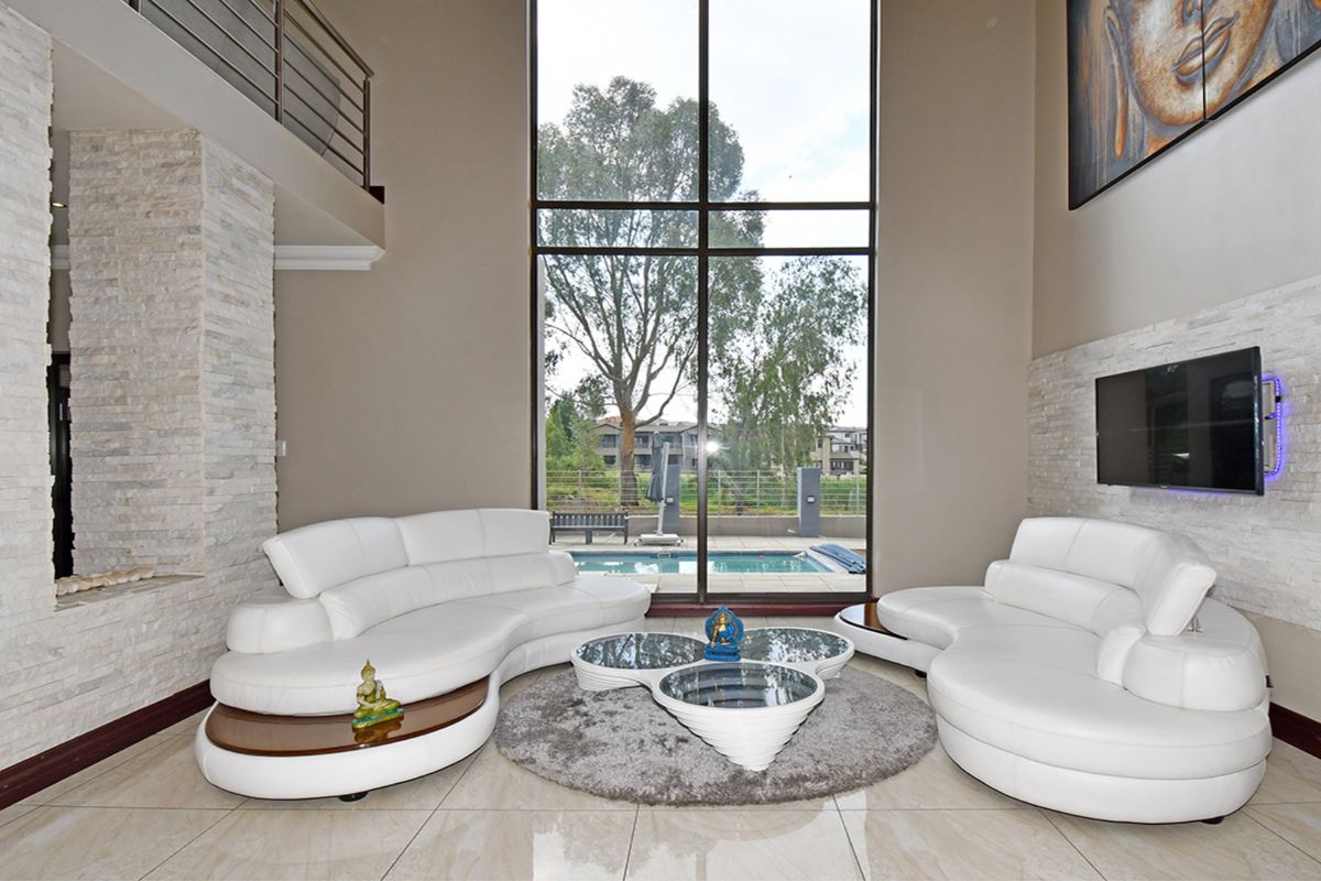 Spacious double-volume living room featuring stone cladding, large windows with pool views, and elegant tiled flooring.
