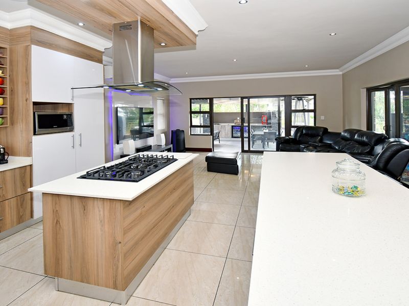 Modern open-plan kitchen and living area featuring a large island with gas cooktop, sleek cabinetry, tiled floors, and seamless access to the outdoor patio.