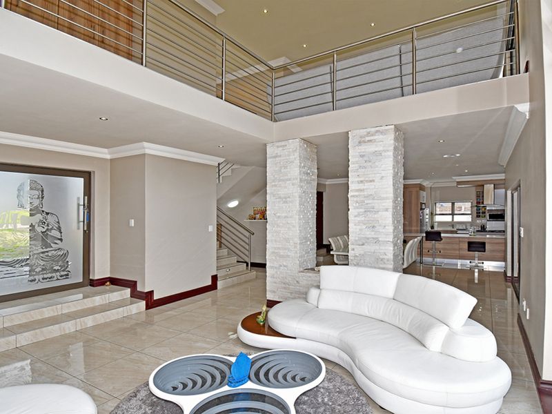 Spacious open-plan living area featuring double-volume ceilings, a mezzanine level with stainless steel balustrades, and striking stone-clad feature columns.