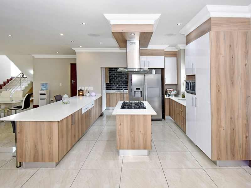 Modern open-plan kitchen featuring a central island with gas cooktop, high-gloss cabinetry, stone countertops, and integrated appliances, flowing into the dining area.