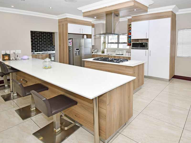 Modern kitchen featuring a large island with stone countertops, gas hob, integrated appliances, and sleek cabinetry with recessed lighting.