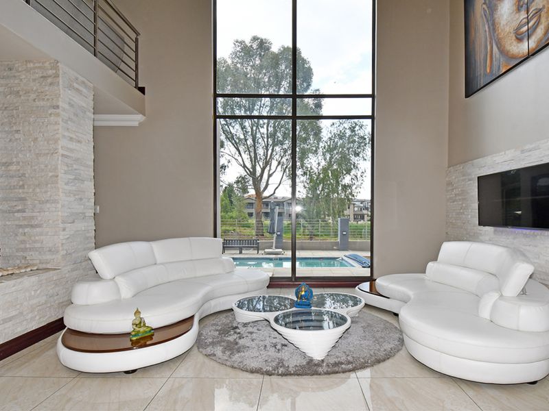 Spacious double-volume living room featuring stone cladding, large windows with pool views, and elegant tiled flooring.
