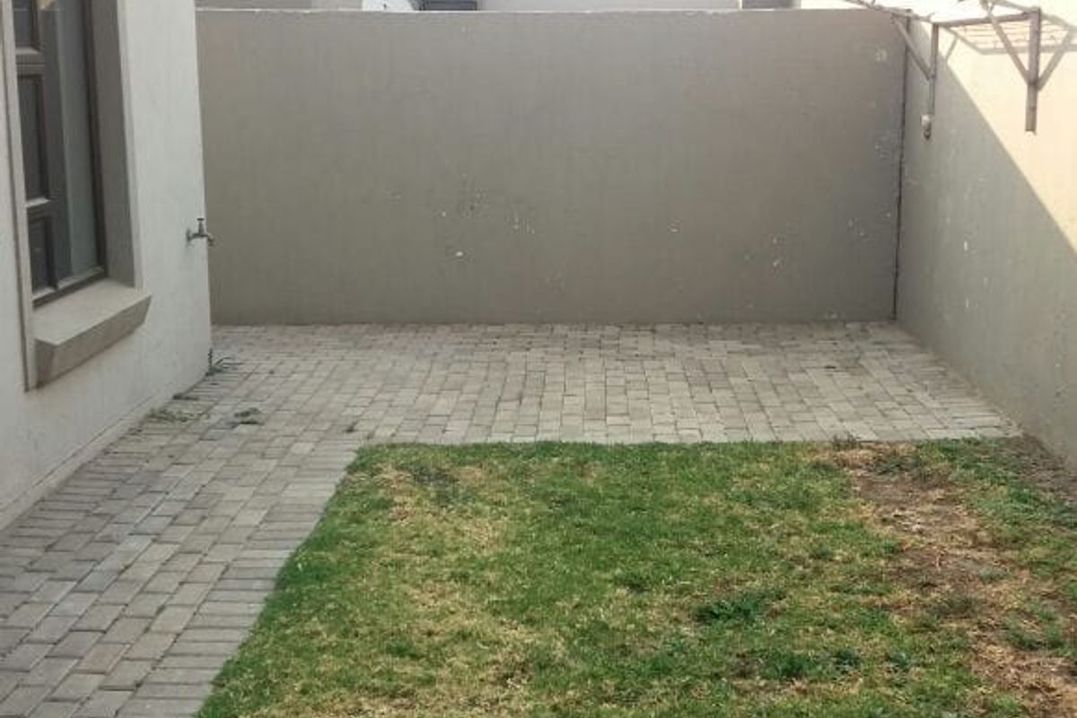 A private rear courtyard featuring a paved patio area, a small lawn, and a wall-mounted drying rack, enclosed by high boundary walls.