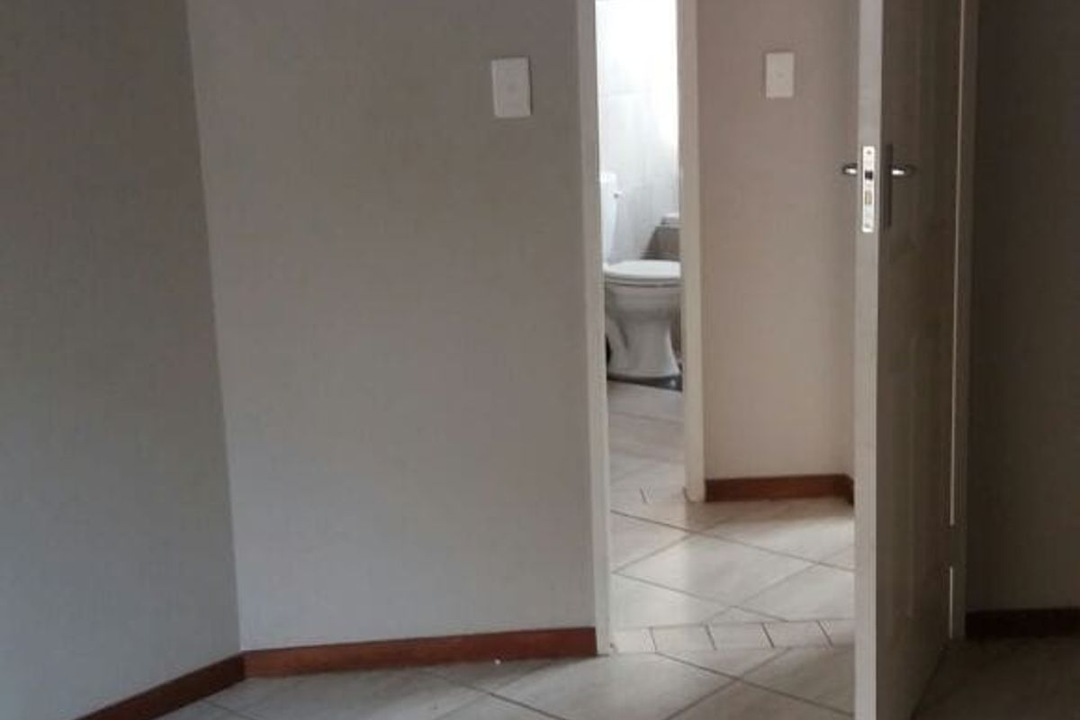 An empty bedroom featuring neutral tiled flooring and a doorway leading to an adjacent bathroom.