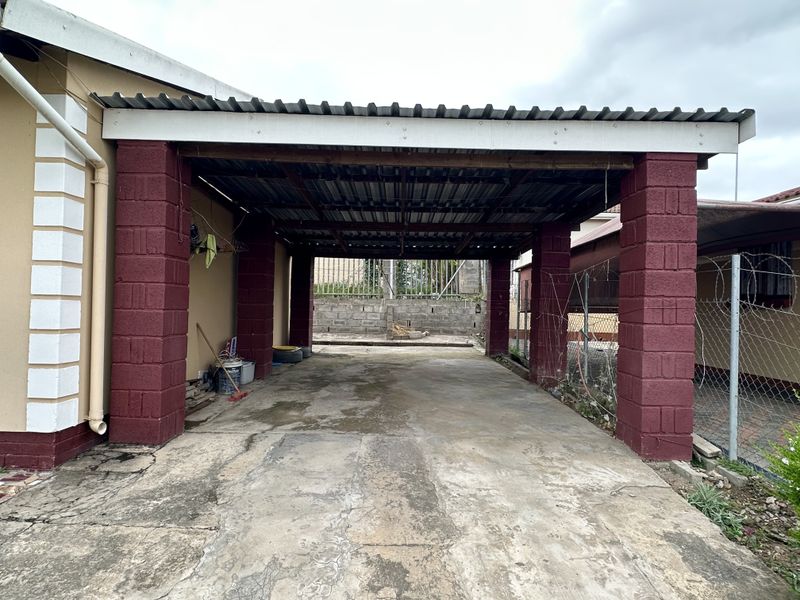 A covered carport area featuring a corrugated metal roof supported by brick pillars and a concrete driveway.