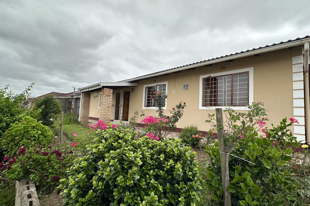 Rear view of a single-story house featuring a paved walkway, established garden, and security bars on the windows.