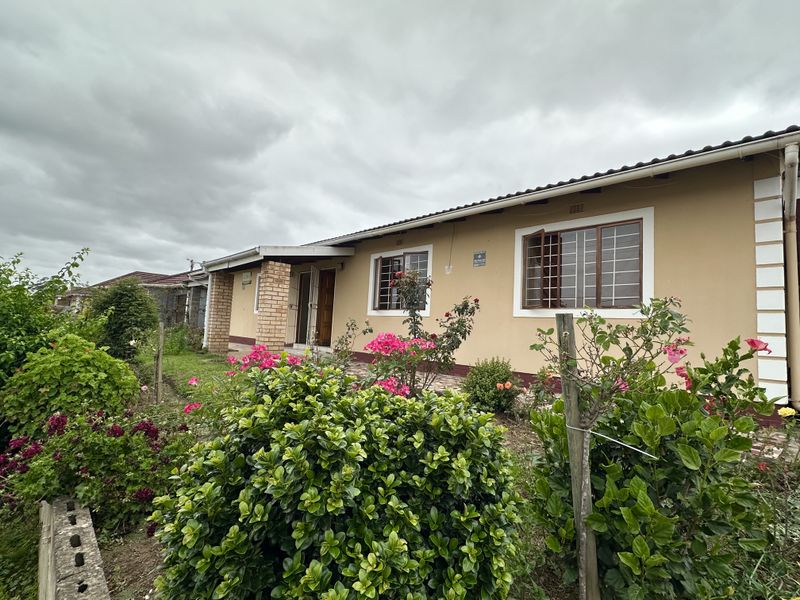 Rear view of a single-story house featuring a paved walkway, established garden, and security bars on the windows.