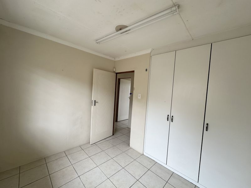 An empty bedroom featuring tiled flooring, built-in cupboards, and a fluorescent light fixture, requiring cosmetic updates to improve its overall condition.
