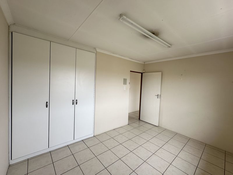 An empty bedroom featuring tiled flooring, built-in cupboards, and a neutral color palette, offering a blank canvas for personalization.