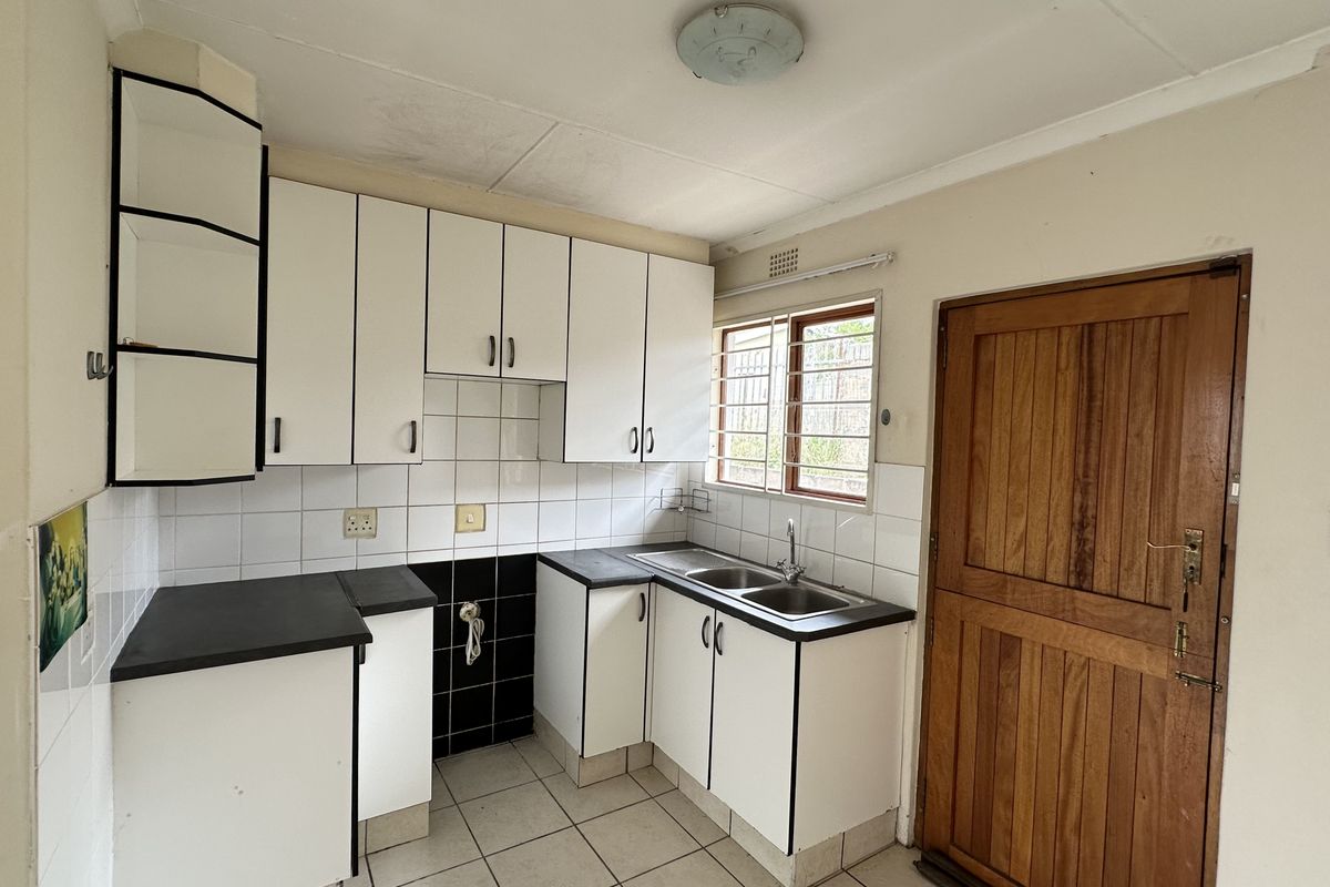 A functional kitchen featuring white built-in cabinetry, a double basin sink, tiled flooring, and a solid wooden door leading to the exterior.