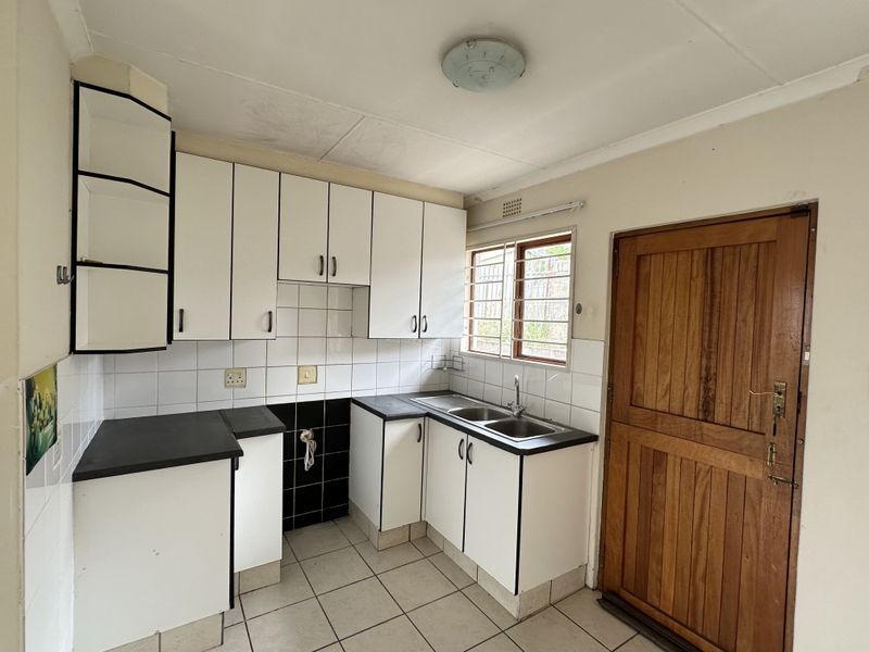 A functional kitchen featuring white built-in cabinetry, a double basin sink, tiled flooring, and a solid wooden door leading to the exterior.