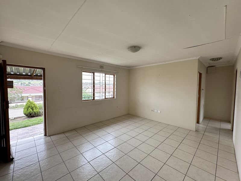 An empty living room featuring tiled flooring, security bars on the windows, and direct access to the exterior.