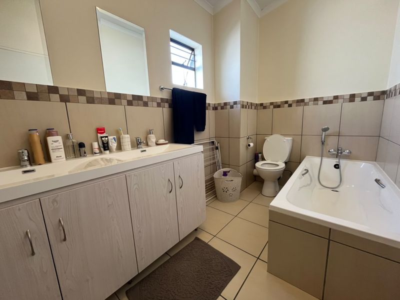 A functional bathroom featuring a double vanity cabinet, a bathtub with a handheld shower attachment, a toilet, and neutral tiled finishes.