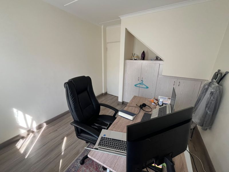 A functional home office space featuring light wood-look laminate flooring and custom built-in cabinetry tucked under the staircase.