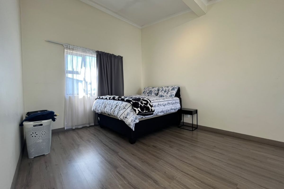 A spacious bedroom featuring modern laminate flooring, neutral wall tones, and a window with installed curtain rails.