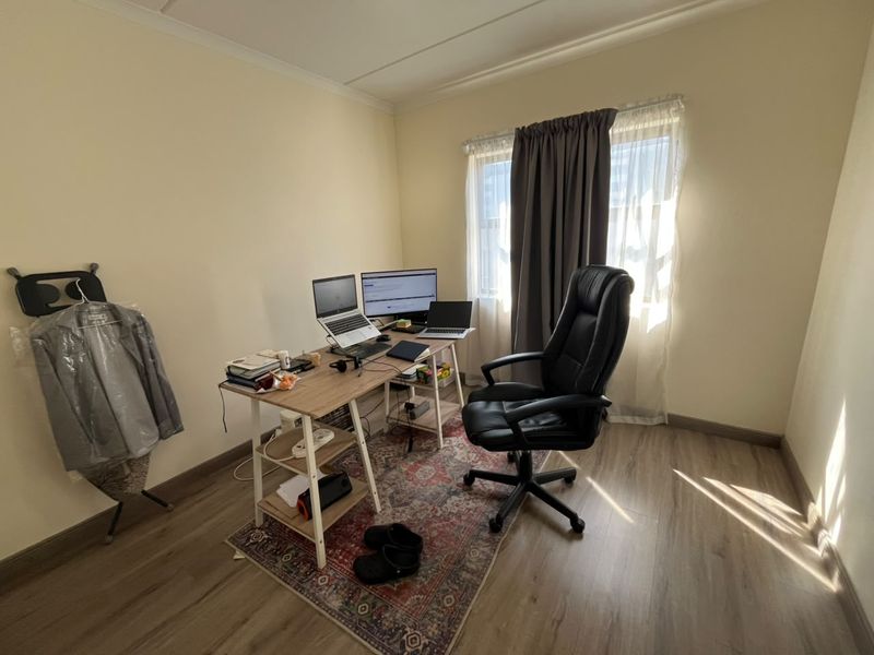 A functional home office space featuring laminate flooring and natural light from a window with curtain treatments.