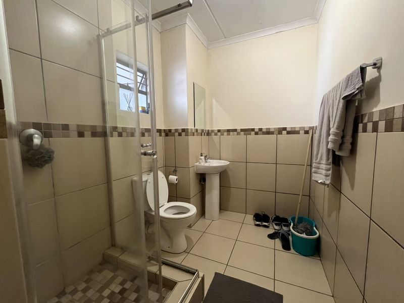 A functional bathroom featuring a pedestal basin, toilet, and a glass-enclosed shower with neutral wall and floor tiling.