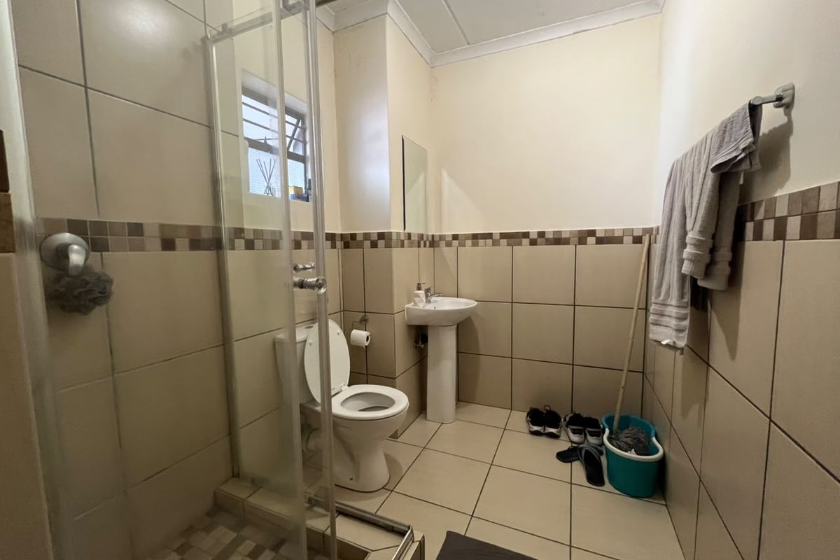 A functional bathroom featuring a pedestal basin, toilet, and a glass-enclosed shower with neutral wall and floor tiling.