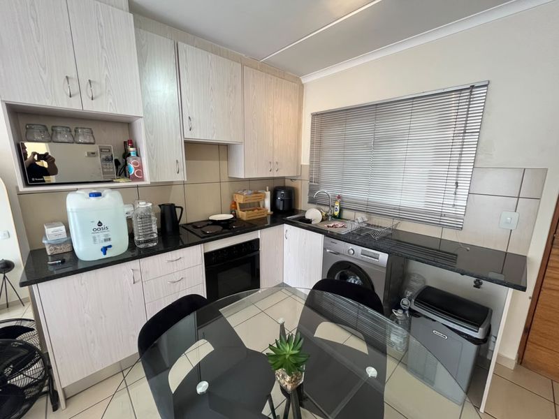 A functional kitchen featuring light wood-grain cabinetry, granite countertops, integrated oven and hob, and tiled flooring with a dedicated space for a washing machine.