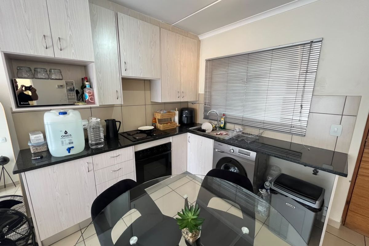 A functional kitchen featuring light wood-grain cabinetry, granite countertops, integrated oven and hob, and tiled flooring with a dedicated space for a washing machine.